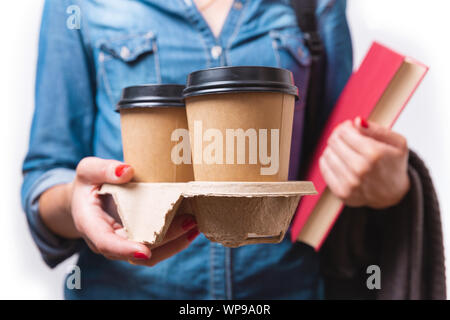 Two paper to go coffee cups in women's hand. Student with takeaway coffee cups and book in her hands Stock Photo
