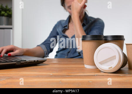 Tired businesswoman in the office with many to go coffee cups on the table Stock Photo