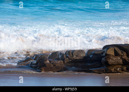 Tide is in. Colorful seascape. Vicious waves crashing against the shoreline on a sunny afternoon.  There is a small rocky crop in the foreground Stock Photo