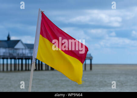 A lifeguard flag marking the safe swimming area with Southwold pier behind. Stock Photo