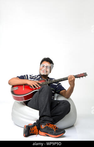 Young man playing guitar with sitting on bean bag Stock Photo
