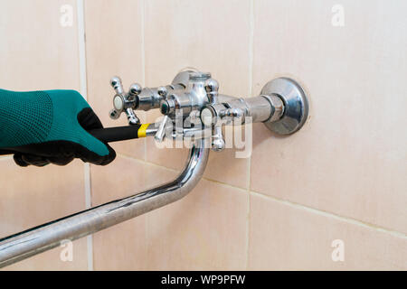 A gloved hand with a wrench repairs the faucet in the bathroom Stock Photo