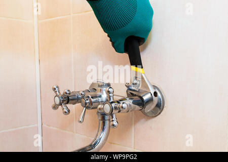 A gloved hand with a wrench repairs the faucet in the bathroom Stock Photo