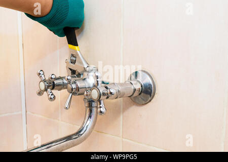 A gloved hand with a wrench repairs the faucet in the bathroom Stock Photo