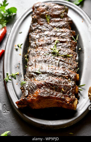 Close up of hot grilled spare ribs on plate over black stone background. Tasty bbq meat. Stock Photo