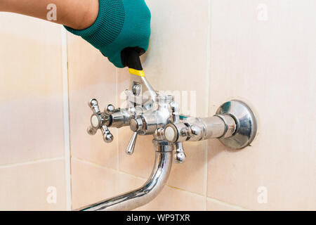 A gloved hand with a wrench repairs the faucet in the bathroom Stock Photo