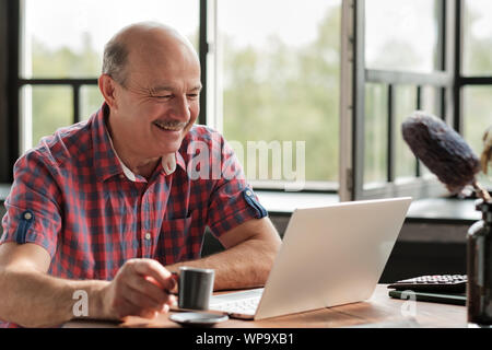 Senior hispanic man smiling looking on laptop screen at the living room Stock Photo