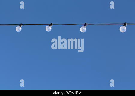 4 round textured light bulbs hanging from a wire with a clear blue sky background Stock Photo