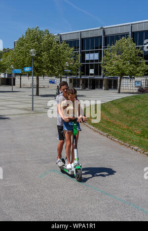 Teenage couple on a Lime electric scooter in part of the Munich 1972 Olympic Park, Munich, Bavaria, Germany. Stock Photo