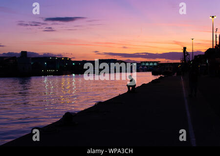 Man sitting on the edge of Poole Quay in evening sunlight, Poole, Poole Harbour, Dorset, UK, September Stock Photo