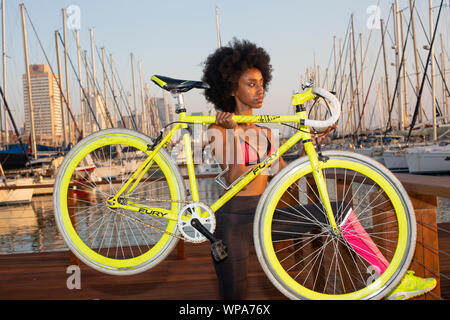 Young female African cyclist resting after an outdoor workout. The yachts in the Tel Aviv Marina the background Stock Photo