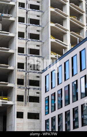 Skeleton frame of an office building skyscraper under construction with part of another one already built, modern urban architecture. Stock Photo