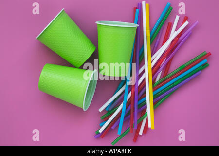 Multi-colored plastic disposable cups and straws on a pink table background. Colorful cocktail tubes. Stock Photo