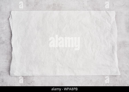 Crumpled piece of white parchment or baking paper on grey concrete background. Top view. Copy space for text and design element. Stock Photo