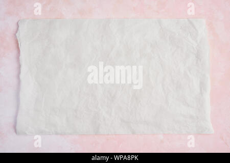 Crumpled piece of white parchment or baking paper on rose and white texture pattern background. Top view. Copy space for text and design element. Stock Photo