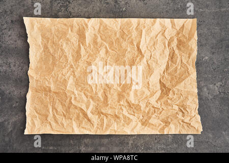 Crumpled piece of brown parchment or baking paper on black concrete background. Top view. Copy space for text and design element. Stock Photo