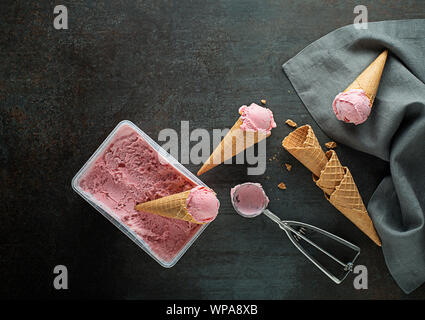 Fresh of soft ice cream or frozen yogurt with berry fruit flavours. Fruit ice cream scoops, scooped out of container in to waffle cones with a silver Stock Photo