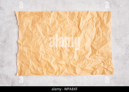 Crumpled piece of brown parchment or baking paper on grey concrete background. Top view. Copy space for text and design element. Stock Photo