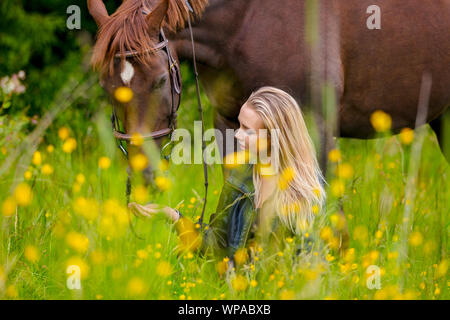 Woman sitting and talking in the meadow feeding her arabian horse Stock Photo