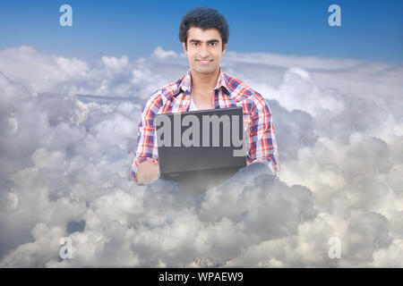 Young man sitting on clouds and working on a laptop Stock Photo