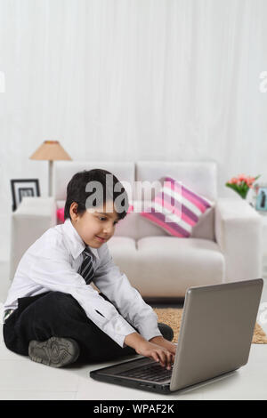 Schoolboy sitting on floor and using laptop at home Stock Photo