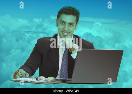 Young man sitting on clouds and using a laptop Stock Photo