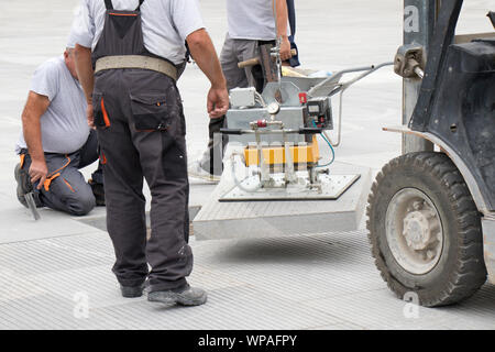 Pavement construction workers lifting the stone slab with vacuum magnet device, block paving equipment machinery Stock Photo