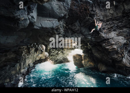 man climbing above the ocean in a volcanic cave Stock Photo