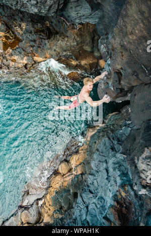 Man climbing above the ocean in a volcanic cave Stock Photo