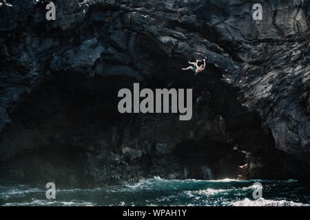 man climbing above the ocean in a volcanic cave Stock Photo