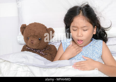 Little girl is coughing and sore throat lying on bed with toy bear, Health care concept Stock Photo