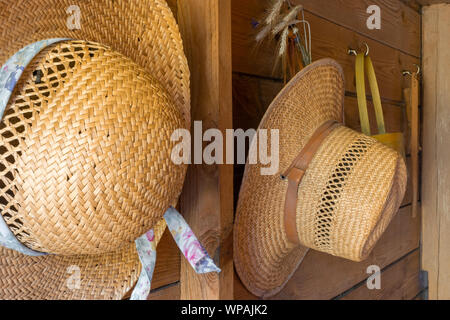 Straw hats, rye bouquet and wooden basket hanging on wooden wall of countryside house Stock Photo