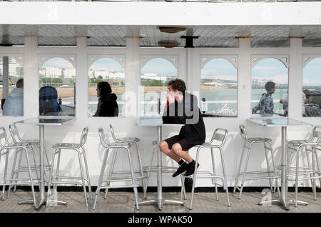 Young man sitting alone at a table on a rainy day on Brighton Pier in East Sussex England UK  KATHY DEWITT Stock Photo