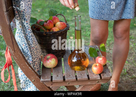 A bottle of apple cider vinegar with fresh fruit, with a woman in the background Stock Photo