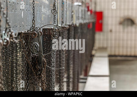 Close up group of hanging small chains inside old abandon factory or industrial building. Detail of machinery parts, chains hang on partition board. Stock Photo