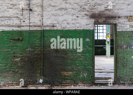 Front view of rough old scratch painted with white and green brick wall, damage electric cables and rectangular door in abandon industrial building. Stock Photo