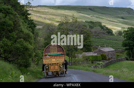 Bow Top Gypsy caravan pulled by two horses followed by a flat bed cart, travelling down Mallerstang on the way to Appleby horse fair. UK. Stock Photo