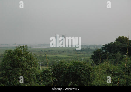 Two modern skyscrapers in misty background with green african woodland in foreground, high angle view. Stock Photo