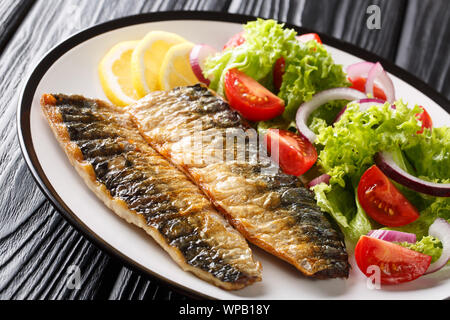 Portion of grilled mackerel fillet with lemon and fresh vegetable salad close-up on a plate on the table. horizontal Stock Photo