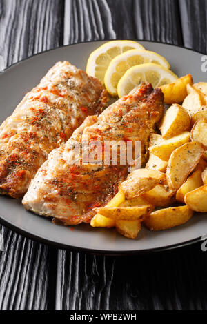 Spicy tasty grilled mackerel filet with potato wedges and lemon close-up on a plate on the table. vertical Stock Photo