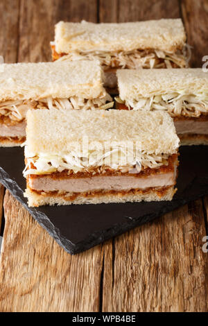 Sliced japanese katsu sando sandwiches with tonkatsu sauce and cabbage closeup on a slate board on a wooden table. vertical Stock Photo