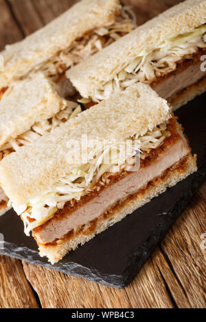 Homemade tender katsu sando sandwiches with tonkatsu sauce and cabbage close-up on a slate board on the table. vertical