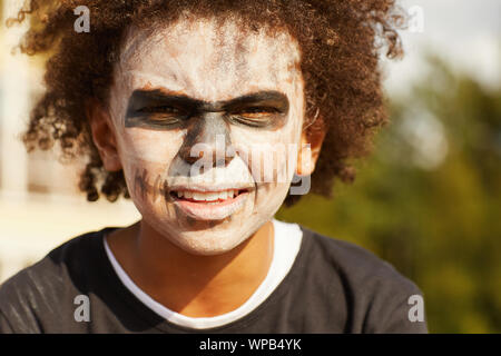 Head and shoulders portrait of tough African-American boy wearing skeleton costume posing outdoors on Halloween, lit by sunlight Stock Photo