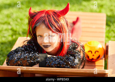 Portrait of cute girl wearing Halloween costume posing outdoors in sunlight while trick or treating, copy space Stock Photo