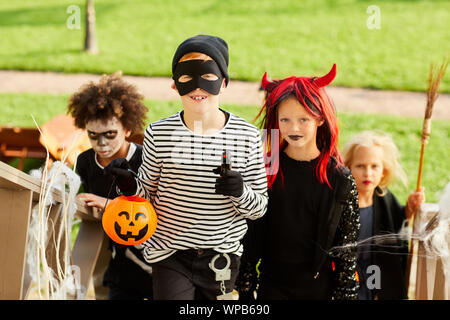 Multi-ethnic group of children trick or treating on Halloween standing on stairs in row, focus on smiling boy wearing costume and holding pumpkin basket Stock Photo