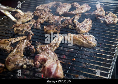 Lovely lamb being grilled and barbecued on an open fire heated with charcoal and silver thongs turning the chops over as it cooks. Stock Photo