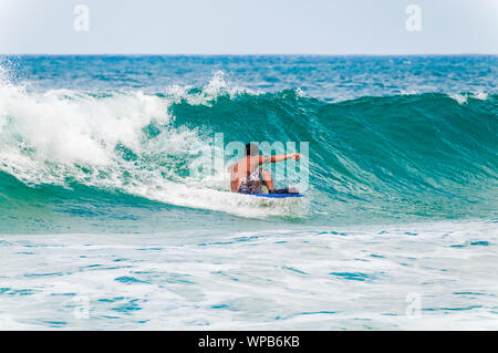 KOLOA, KAUAI, HI - APRIL 24, 2008 - Young man riding a boogie board in a blue wave in the summer. Stock Photo