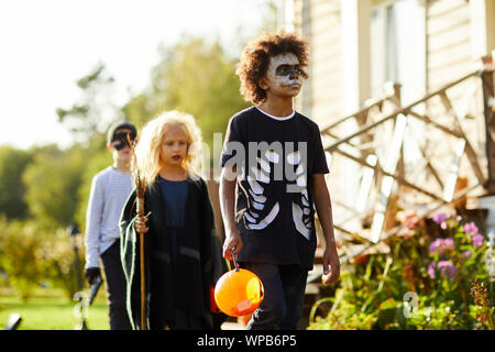 Multi-ethnic group of children trick or treating on Halloween, focus on African-American boy wearing costume and holding basket, copy space Stock Photo