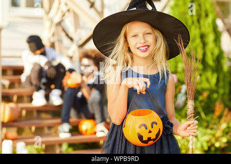 Waist up portrait of cute little girl wearing Halloween costume looking at camera while posing outdoors holding pumpkin basket, copy space Stock Photo