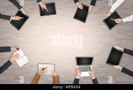 Group of people with devices in hands having desk discussion and making reports together on laptop, tablet, notebook Stock Photo